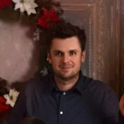 Portret mężczyzny w koszuli w kropki na tle dekoracji świątecznej w ramie. Uśmiechnięty, z krótkimi włosami i ciemnymi oczami. Naturalne światło.