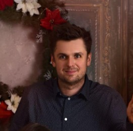 Portret mężczyzny w koszuli w kropki na tle dekoracji świątecznej w ramie. Uśmiechnięty, z krótkimi włosami i ciemnymi oczami. Naturalne światło.