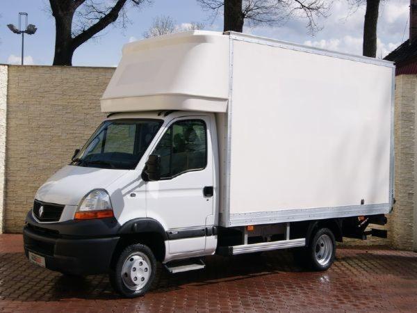 Biały samochód dostawczy Renault Master z zabudową kontenerową, zaparkowany na kostce brukowej przed ceglanym murem.