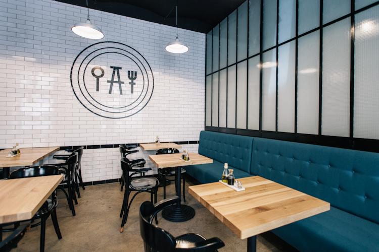 Wnętrze restauracji w Kłobucku z drewnianymi stolikami, czarnymi krzesłami, niebieską tapicerowaną ławą i białymi ścianami z cegieł z logo firmy.