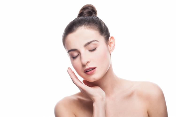 Portret kobiety z zamkniętymi oczami, delikatnie dotykającej policzka, włosy upięte w kok na białym tle.