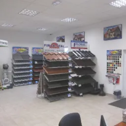 Ekspozycja różnorodnych pokryć dachowych w salonie sprzedaży, prezentująca blachodachówki, dachówki ceramiczne i blachę trapezową różnych producentów, w tym Finco-Stal, Florian i Blachy Pruszyński,...