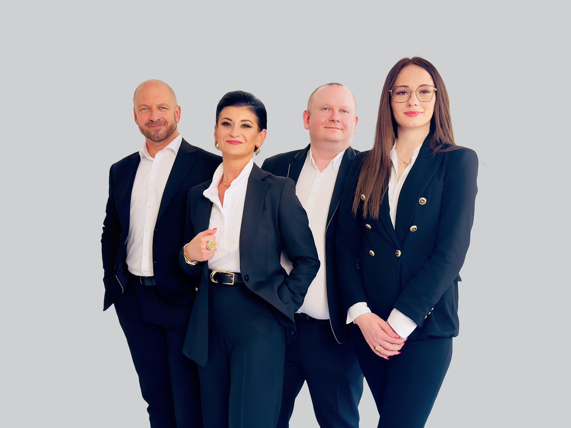 Zespół doradców finansowych w eleganckich strojach biznesowych pozuje na jasnym tle. Uśmiechnięte twarze, profesjonalny wizerunek, złote akcenty w biżuterii.