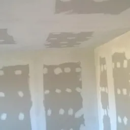 Pokój w trakcie prac wykończeniowych: ściany i sufit po szpachlowaniu, z widocznymi miejscami po łatach i punktowym szpachlowaniu. Przygotowanie do malowania.