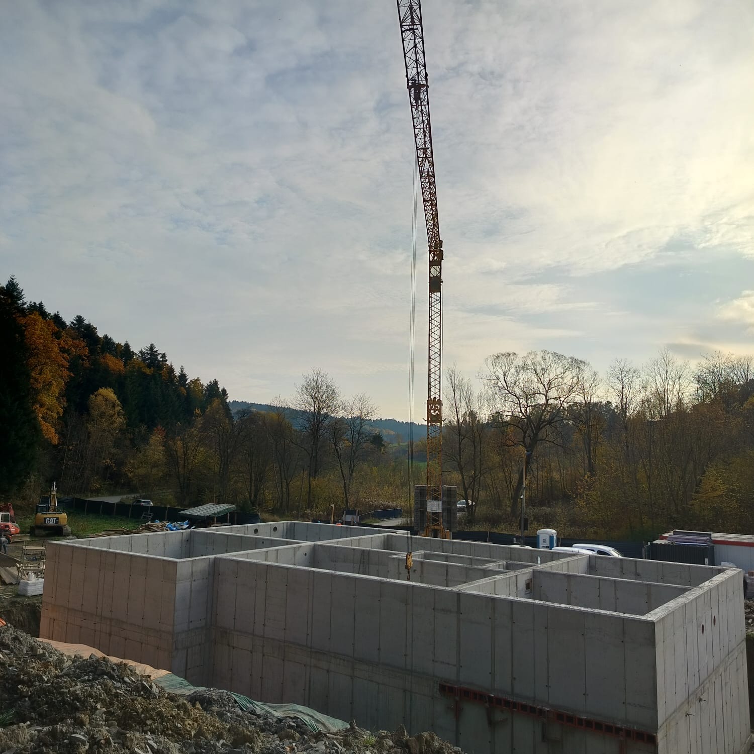 Wylane betonowe ściany fundamentowe z podziałem na pomieszczenia, widok z góry, na tle jesiennego krajobrazu i żurawia budowlanego.