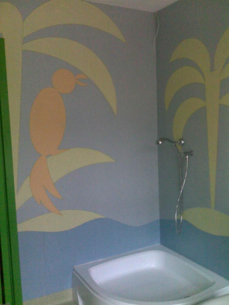 Ściana w łazience z ręcznie malowanymi palmami i papugą w pastelowych kolorach, nad wanną, widoczny kran.