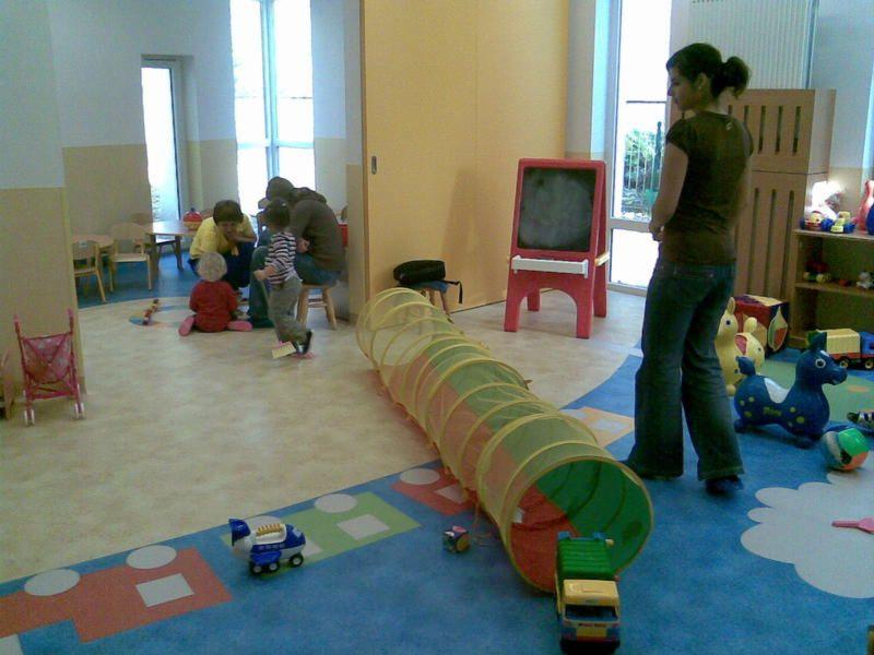 Kolorowa wykładzina podłogowa w pokoju zabaw dla dzieci z tunelem, zabawkami i osobami w tle.