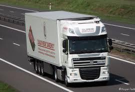 Biała ciężarówka z zabudową chłodniczą jadąca autostradą. Na boku naczepy widoczne logo firmy i napis 'SUPER CONCEPT'.