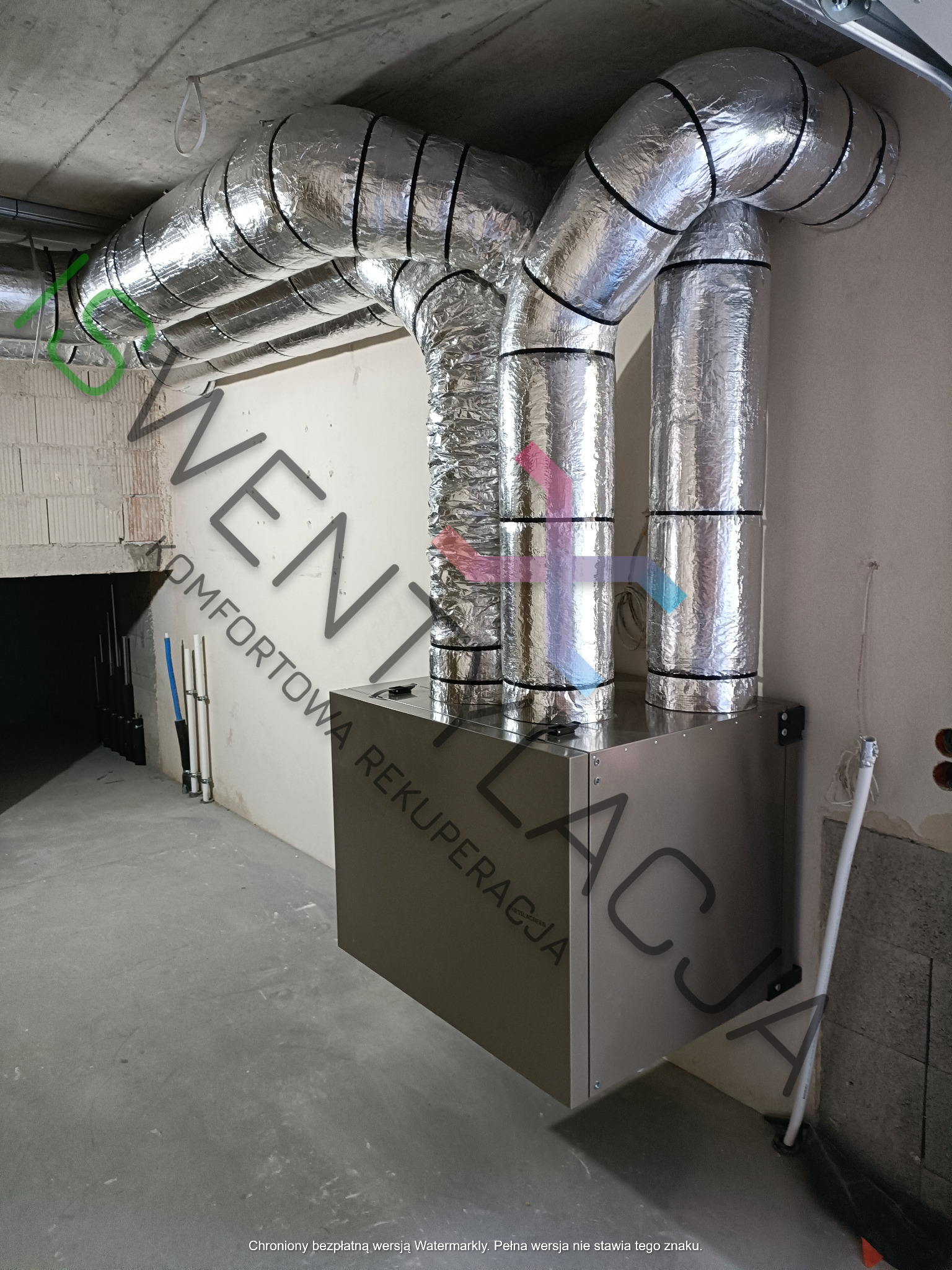 Centrala wentylacyjna z izolowanymi przewodami w surowym wnętrzu, widoczne niedokończone ściany i sufit.