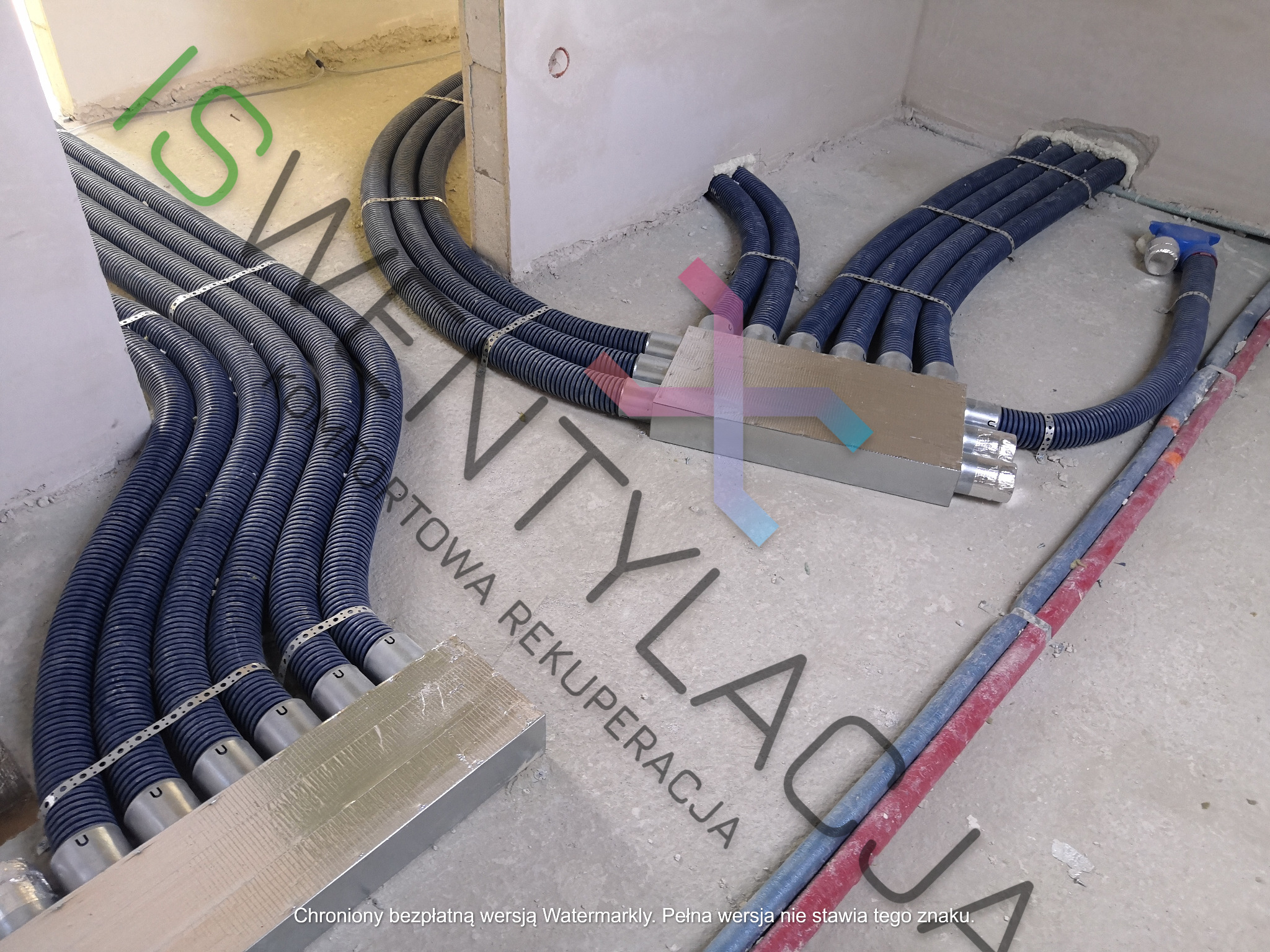 Rozprowadzenie przewodów wentylacyjnych rekuperacji pod posadzką w Mogilanach, widoczne niebieskie rury karbowane i metalowe skrzynki rozdzielcze.