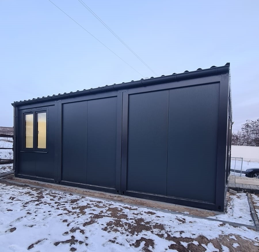 Czarny dom modułowy z oknem w zimowym krajobrazie, widok z zewnątrz na śniegu.