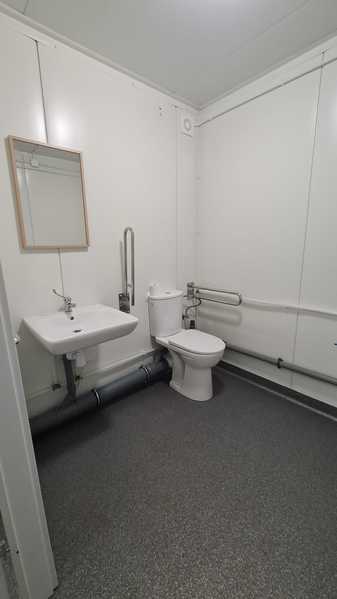 Wnętrze toalety w kontenerze modułowym, z umywalką, lustrem, toaletą i uchwytami dla osób niepełnosprawnych, wykończone w minimalistycznym stylu.