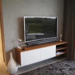 Nowoczesny salon z wiszącą szafką RTV z drewnianym blatem i białymi frontami, minimalistyczną lampką i wazonem w paski.