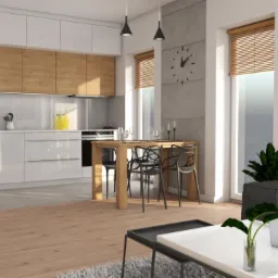 Wnętrze nowoczesnej kuchni z białymi, błyszczącymi szafkami i drewnianymi frontami, połączonej z jadalnią i salonem, oświetlone wiszącymi lampami.