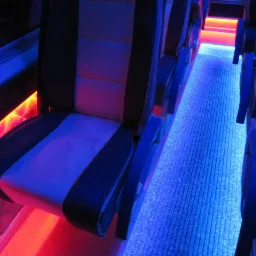 Wnętrze autobusu z podświetlanymi siedzeniami i podłogą w kolorach niebieskim i czerwonym. Nowoczesny design i oświetlenie tworzą unikalny klimat.