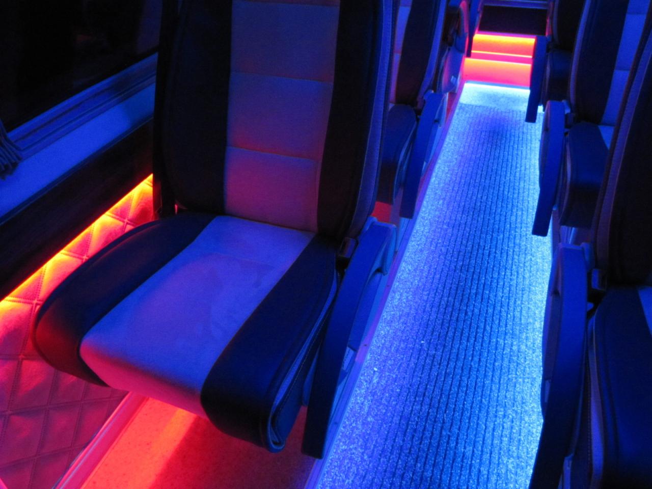 Wnętrze autobusu z podświetlanymi siedzeniami i podłogą w kolorach niebieskim i czerwonym. Nowoczesny design i oświetlenie tworzą unikalny klimat.