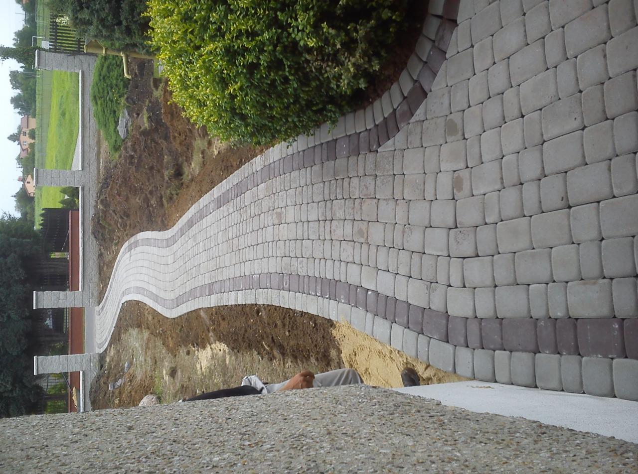 Falujący chodnik z kostki brukowej w odcieniach szarości i brązu, wijący się przez ogród, widok z góry.