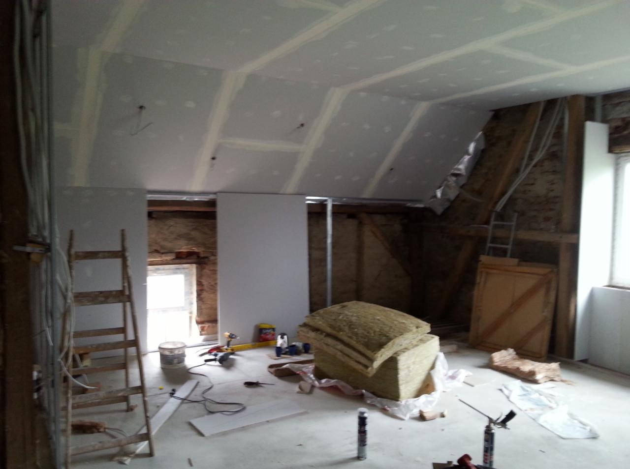 Poddasze w trakcie adaptacji: płyty karton-gips na skosach dachu, ocieplenie wełną mineralną, widoczne narzędzia i drabina. Prace wykończeniowe w surowym stanie.