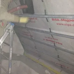 Praca w toku: Docieplenie poddasza z użyciem węża do wdmuchiwania izolacji, widoczna membrana SIGA-Majpell 5 i metalowy stelaż.