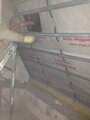 Praca w toku: Docieplenie poddasza z użyciem węża do wdmuchiwania izolacji, widoczna membrana SIGA-Majpell 5 i metalowy stelaż.