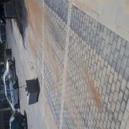 Ułożona kostka brukowa w odcieniach szarości, posypana piaskiem, widok z góry, z zaparkowanymi samochodami w tle.