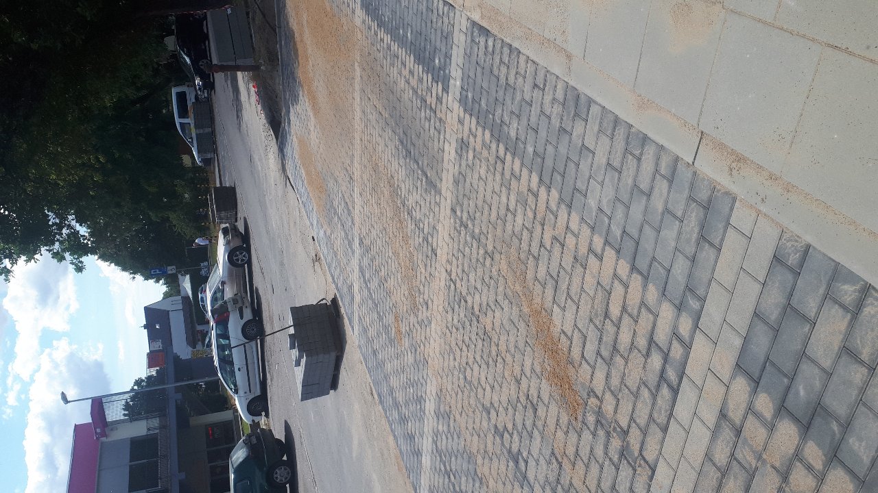 Ułożona kostka brukowa w odcieniach szarości, posypana piaskiem, widok z góry, z zaparkowanymi samochodami w tle.