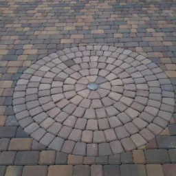Wzór koła ułożony z brązowo-szarych kostek brukowych na powierzchni z kostki w podobnej kolorystyce, centralnie umieszczony szary kamień.
