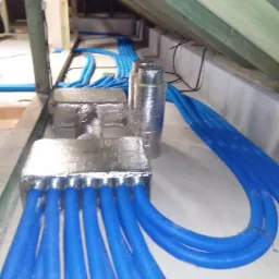 Niebieskie rury w izolacji termicznej ułożone w poddaszu, widoczne drewniane elementy konstrukcyjne dachu.