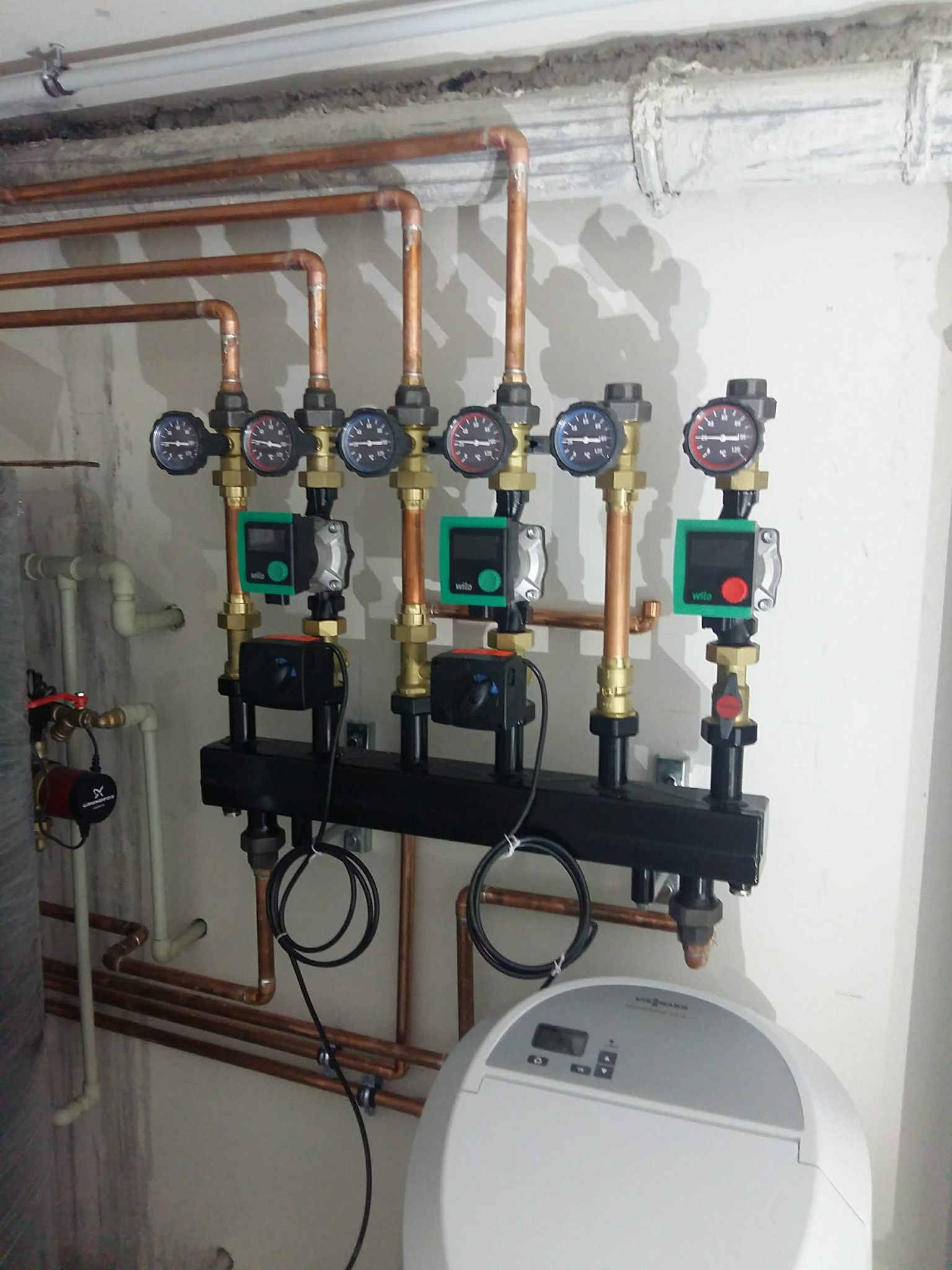 Rozdzielacz z manometrami i pompami obiegowymi, instalacja z miedzianych rur, widoczny zbiornik wyrównawczy Viessmann.