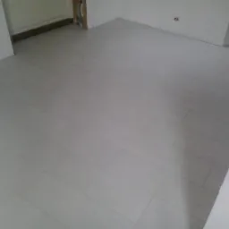 Wykończona podłoga w jasnych, podłużnych panelach przypominających drewno, ułożonych ukośnie w pustym, świeżo wykończonym pomieszczeniu z białymi ścianami i widocznym otworem drzwiowym.