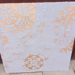 Hubert Szulc wykończenia Wnetrz - Fragment ściany z dekoracyjnym wzorem szablonowym w odcieniach złota i szarości, z widoczną teksturą farby i niedoskonałościami w nałożeniu.