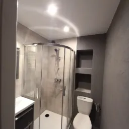 Nowoczesna łazienka z kabiną prysznicową typu walk-in, umywalką z szafką w kolorze grafitowym, toaletą i wnękami w ścianie, wykończona w odcieniach szarości.