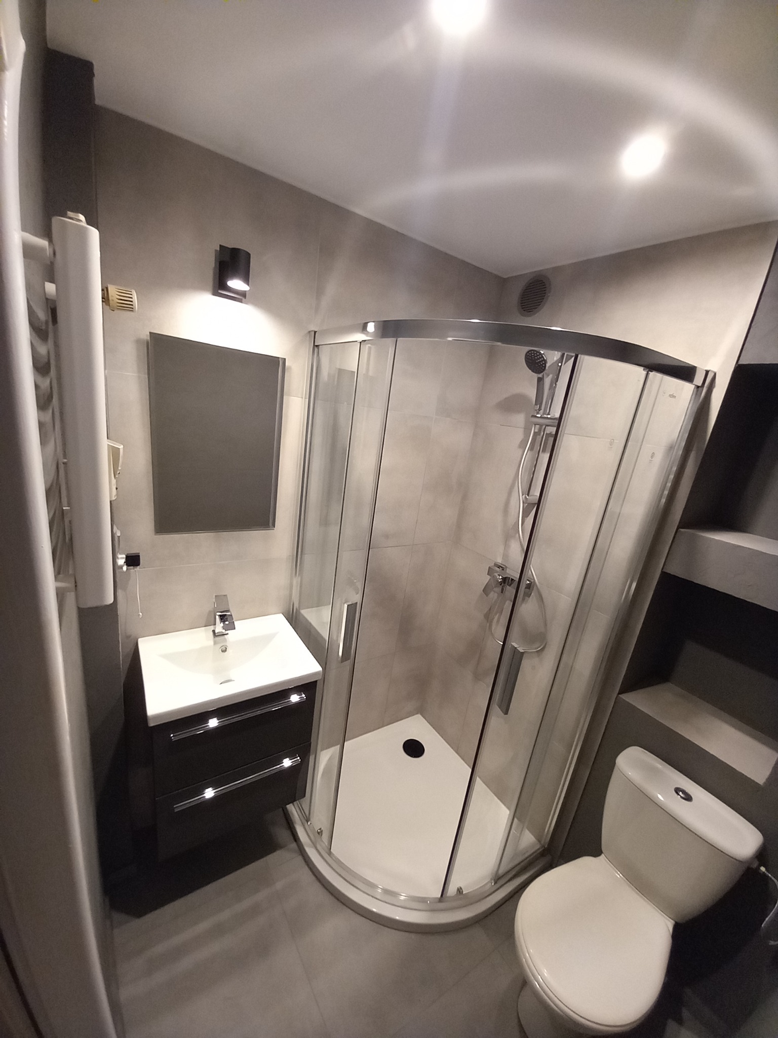 Nowoczesna łazienka w Gostyniu z kabiną prysznicową, umywalką z szafką w kolorze antracytowym, lustrem i grzejnikiem drabinkowym.