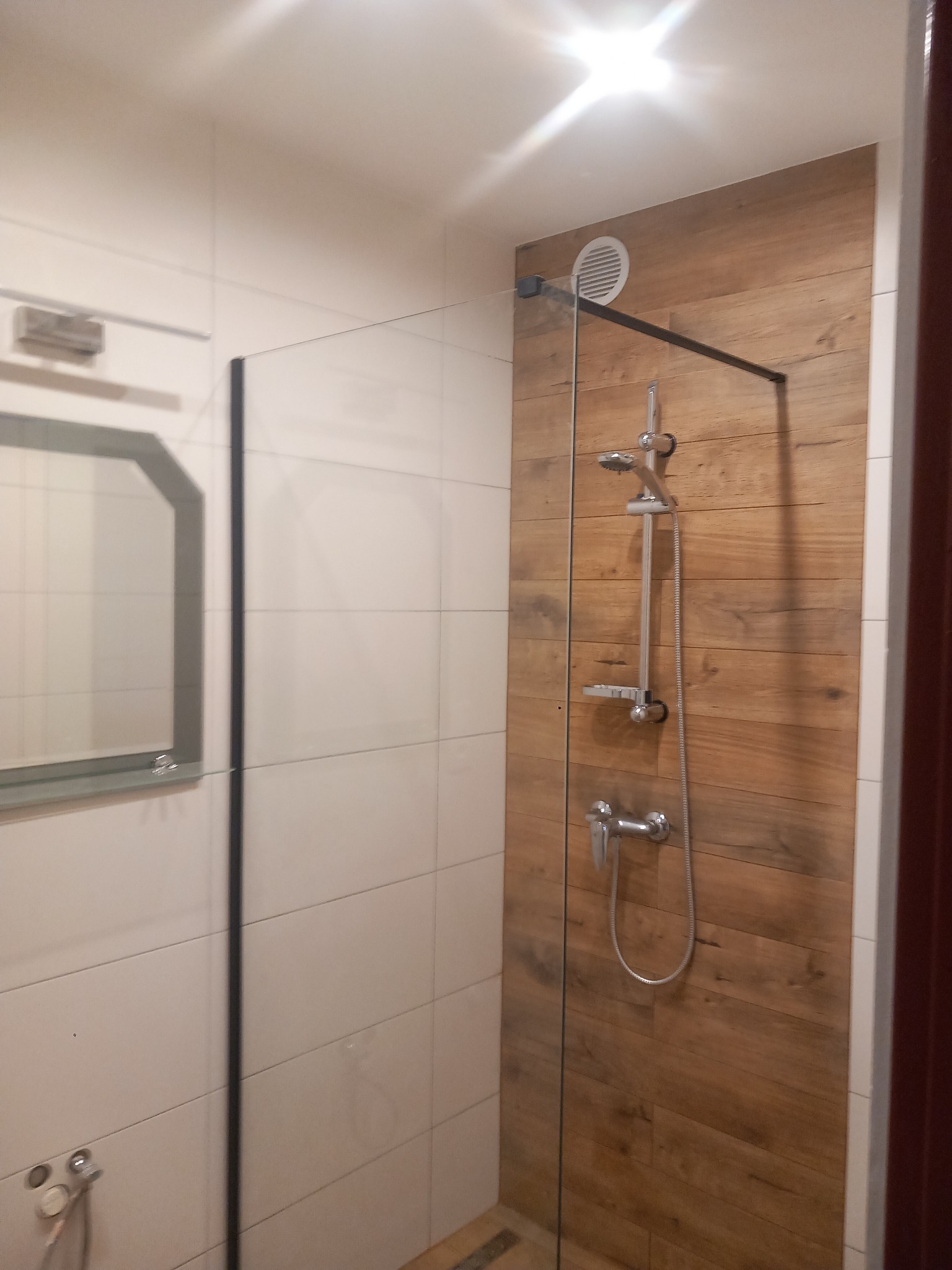 Wykończona łazienka z kabiną prysznicową typu walk-in z drewnopodobną ścianą, chromowaną armaturą i lustrem z podświetleniem LED.