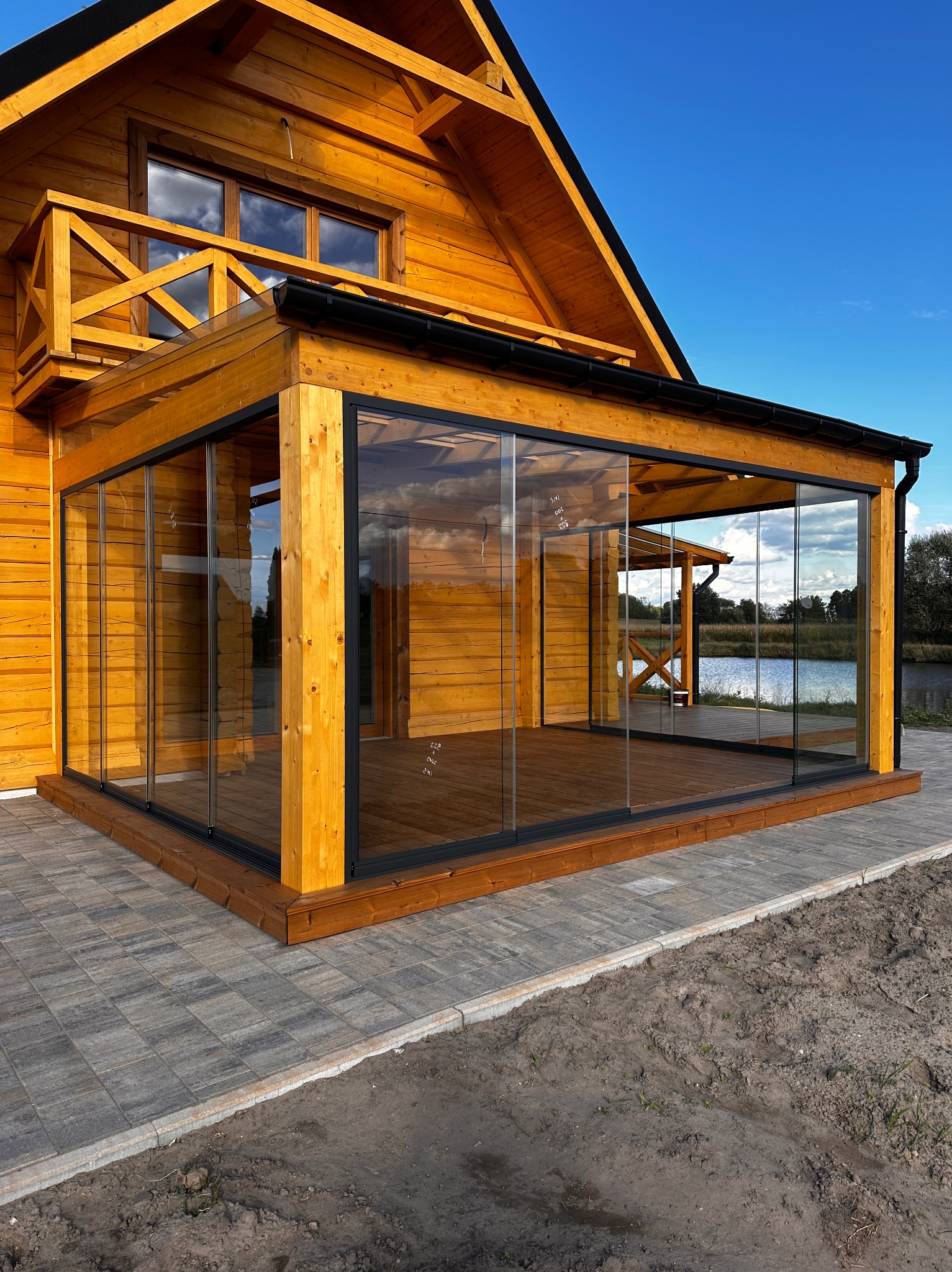 Drewniany dom z przeszklonym tarasem i widokiem na jezioro. Nowoczesna konstrukcja z drewna i szkła, idealna do relaksu na świeżym powietrzu.