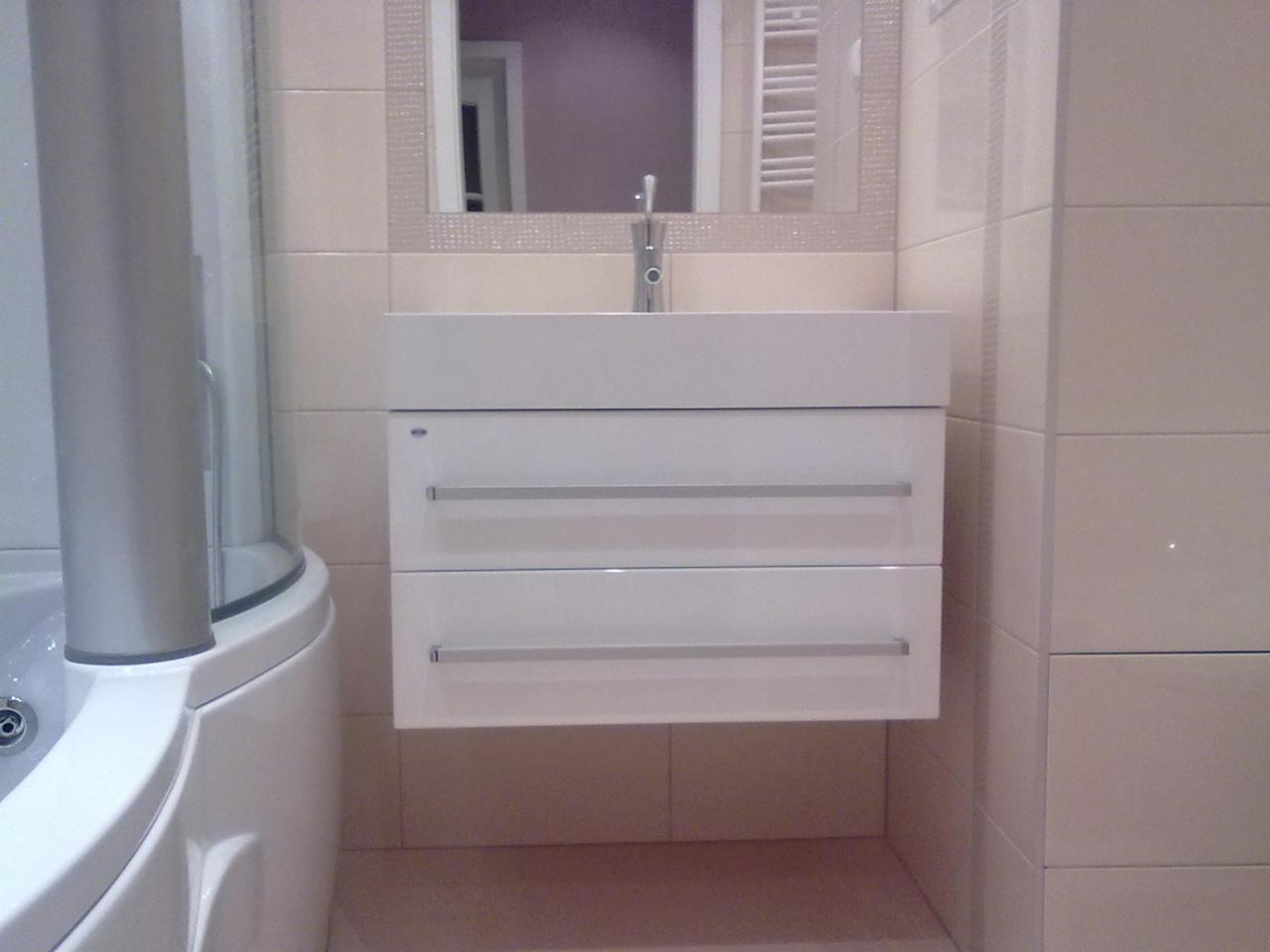 Nowoczesna łazienka z białą, wiszącą szafką umywalkową z dwoma szufladami i lustrem w mozaikowej ramie, obok zaokrąglony narożnik kabiny prysznicowej.