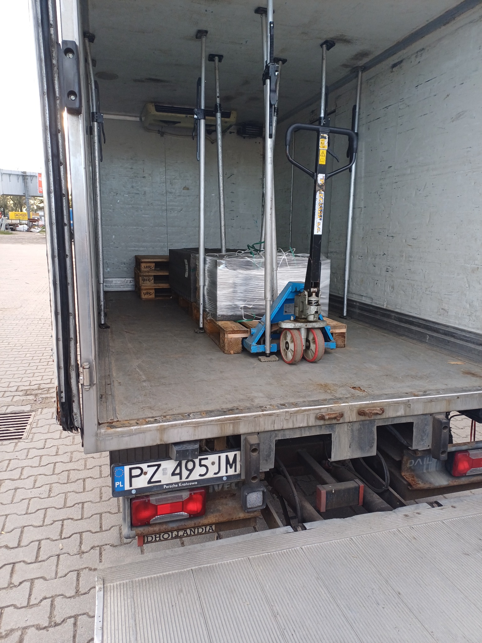 Wnętrze chłodni samochodowej z paletami, zabezpieczonym ładunkiem i wózkiem paletowym w kolorze niebieskim.