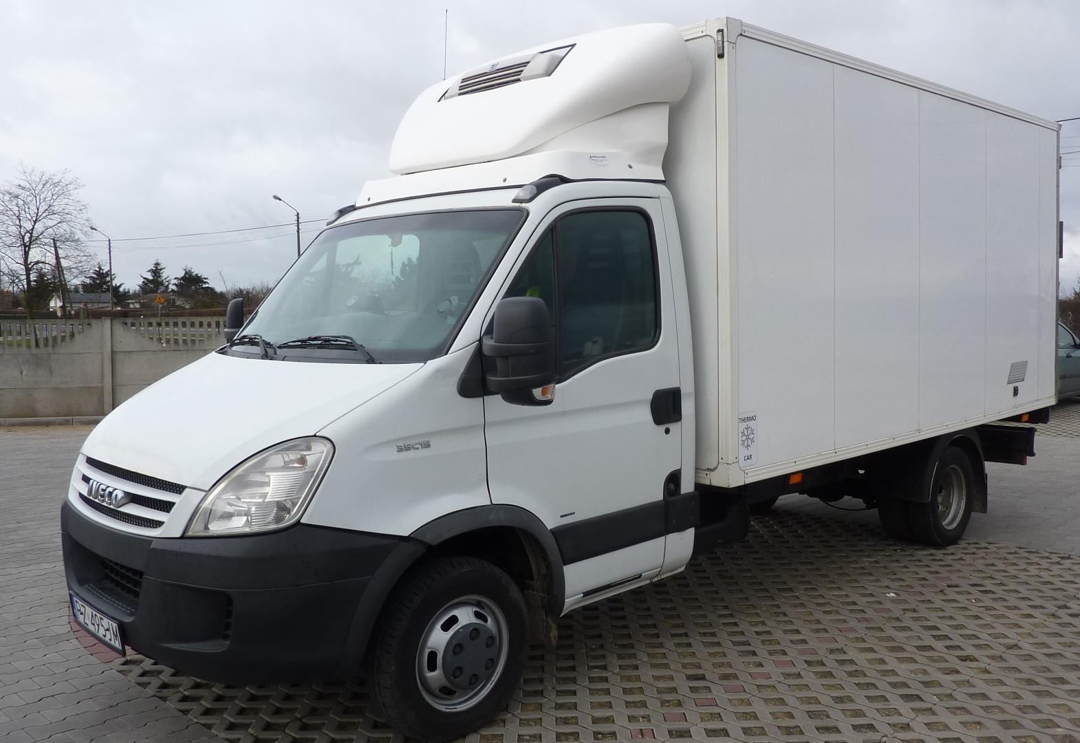 Biały samochód dostawczy Iveco z chłodnią na parkingu z betonowej kostki, widoczny znak 'Thermo Car' na boku.
