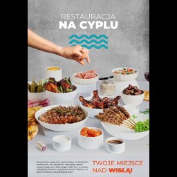 Dawid Jóźwiak REWIR - Bogaty stół z różnorodnymi daniami kuchni restauracji 'Na Cyplu', z ręką wskazującą na potrawy, podkreślający świeżość i lokalne pochodzenie składników.