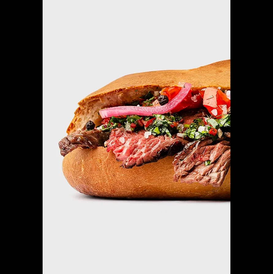 Soczysta kanapka z wołowiną, ziołami i marynowaną cebulą na chrupiącej bułce, sfotografowana z bliska na jasnym tle, eksponująca świeżość składników.