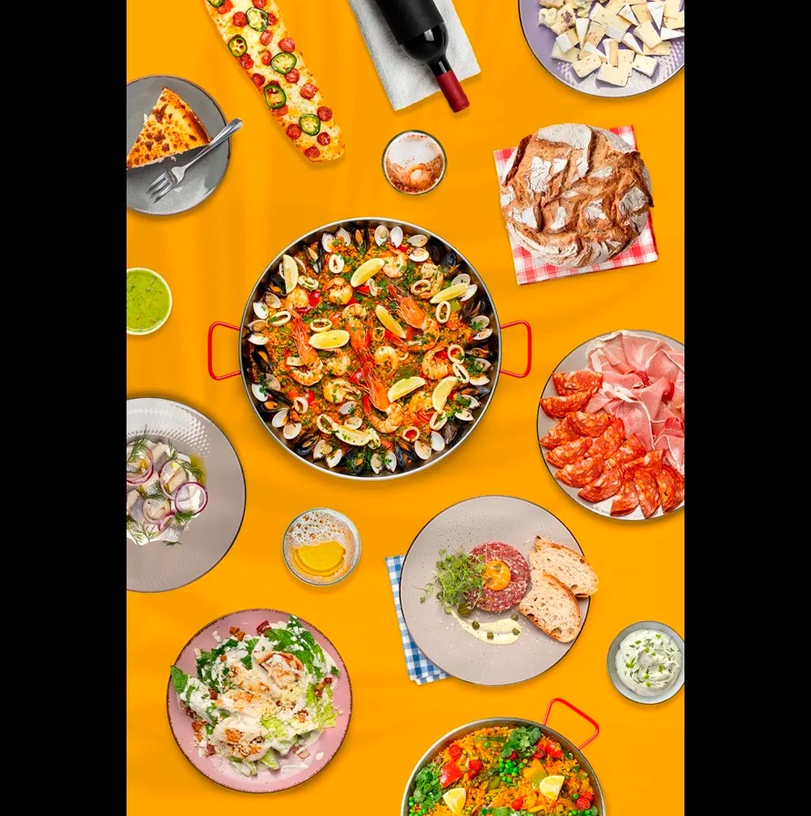 Kompozycja z różnorodnych dań: paella, pieczywo, sałatki, mięsa i sery na żółtym tle. Widok z góry, profesjonalna fotografia kulinarna.