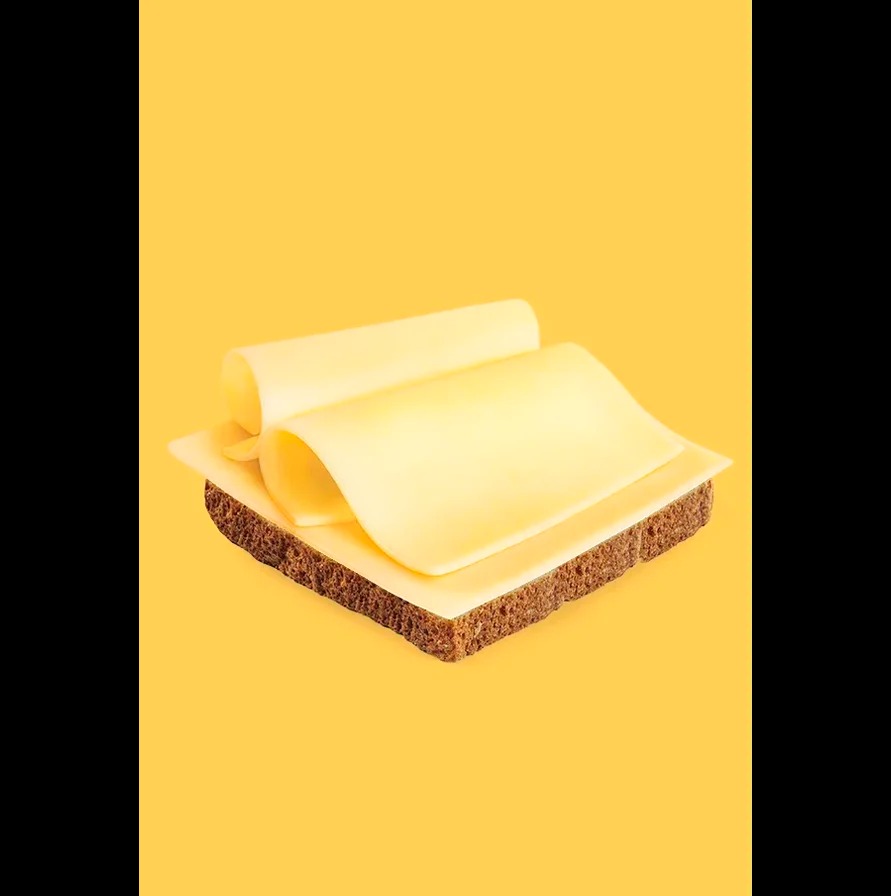 Kanapka z ciemnego pieczywa z serem, dwie rolki sera na wierzchu, na żółtym tle. Minimalistyczna kompozycja, ostre światło, fotografia produktowa.