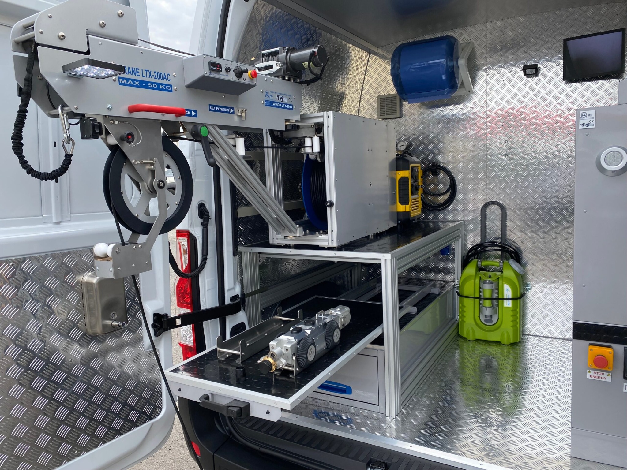 Wnętrze furgonetki serwisowej z profesjonalnym sprzętem do inspekcji i czyszczenia kanalizacji. Widoczny wciągnik, kamera inspekcyjna na wysuwanej półce i inne narzędzia.