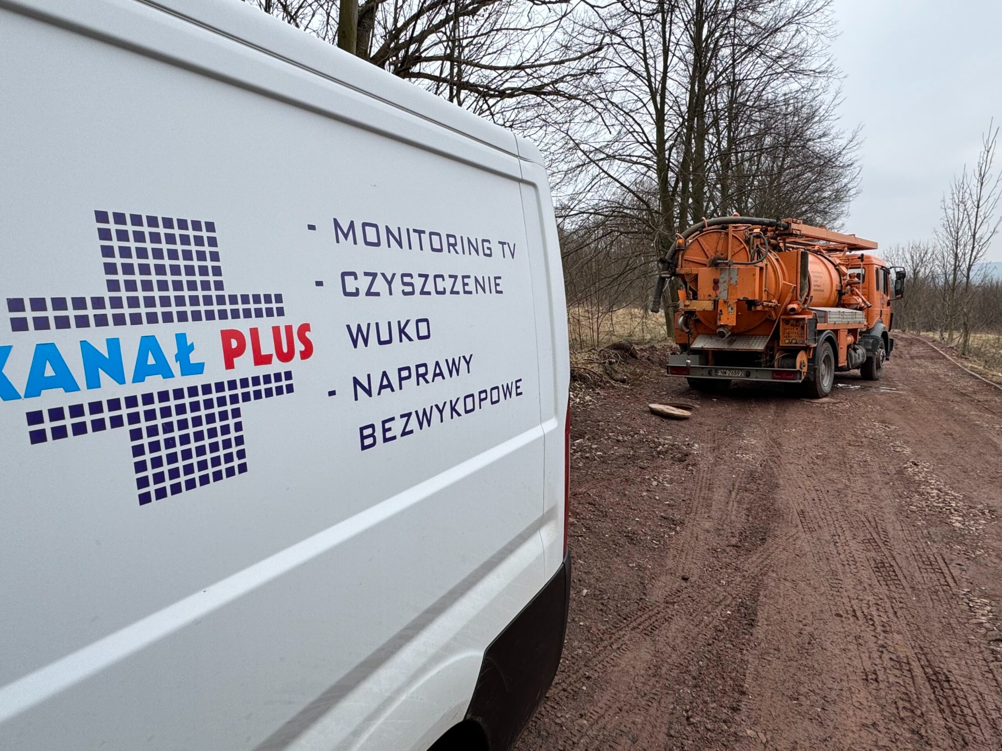 Biały samochód z logo 'Kanał Plus' i hasłami usług. W tle pomarańczowy pojazd asenizacyjny na polnej drodze, sugerujący prace związane z czyszczeniem kanalizacji.