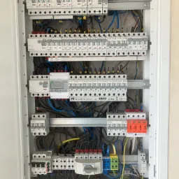 Rozdzielnia elektryczna w białej obudowie, widoczne bezpieczniki, przewody, licznik energii ELS SDM72DR i elementy zabezpieczające Simtec ST30B+C 4P.