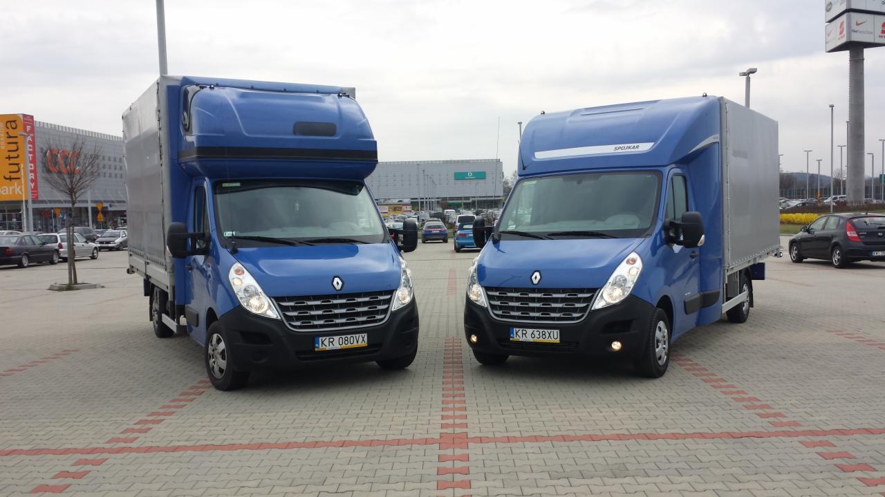 Dwa identyczne, niebieskie busy Renault Master z zabudową plandekową, zaparkowane na parkingu przed centrum handlowym Futura, tablice rejestracyjne KR.
