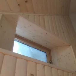 Wykończone drewnianą boazerią poddasze z oknem dachowym, widoczne słoje drewna i detale wykończenia.