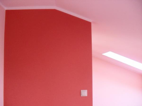Czerwona ściana w skosie poddasza po malowaniu, widoczny włącznik światła i biały pas sufitu. Ściana pomalowana na jednolity kolor, brak dekoracji.