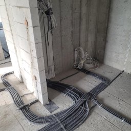 ELMAR TECHNOLOGY SPÓŁKA Z OGRANICZONĄ ODPOWIEDZIALNOŚCIĄ - Układanie peszli elektrycznych w nowym budynku, widoczne kable prowadzone wzdłuż ściany z betonu komórkowego, instalacja w trakcie wykonywania.