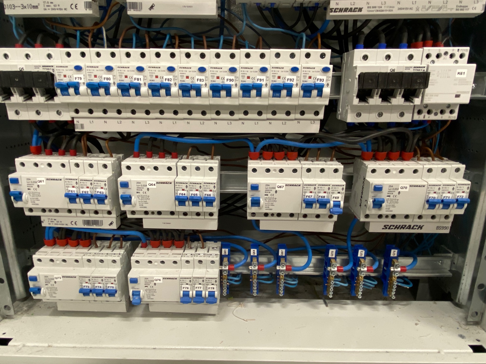 Rozdzielnica elektryczna Schrack z zainstalowanymi bezpiecznikami i przewodami, widoczne oznaczenia faz i numeracja zabezpieczeń.